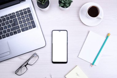 İşyerleri ahşap ofis masaları boş cep telefonları, çeşitli malzemeler. Okul, eğitim, teknoloji ve reklam konsepti. Model yap. Laptop akıllı telefon, bir fincan kahve.