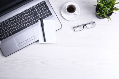 Ofis çalışma alanının en üst görüntüsü, dizüstü bilgisayarı, klavye kalemi, gözlükleri, telefonu, defteri ve kahveyi olan ahşap masa masası..