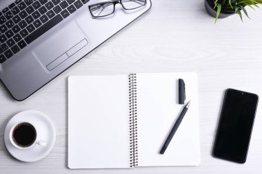 Ofis çalışma alanının en üst görüntüsü, dizüstü bilgisayarı, klavye kalemi, gözlükleri, telefonu, defteri ve kahveyi olan ahşap masa masası..