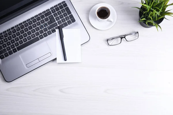 Ofis çalışma alanının en üst görüntüsü, dizüstü bilgisayarı, klavye kalemi, gözlükleri, telefonu, defteri ve kahveyi olan ahşap masa masası..