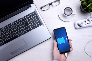 İşyerleri ahşap ofis masaları boş cep telefonları, çeşitli malzemeler. Telefonu şarj ediyor. Model yap. Laptop akıllı telefon, bir fincan kahve.