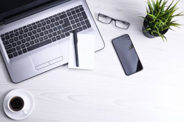 Ofis çalışma alanının en üst görüntüsü, dizüstü bilgisayarı, klavye kalemi, gözlükleri, telefonu, defteri ve kahveyi olan ahşap masa masası..