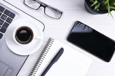 Ofis çalışma alanının en üst görüntüsü, dizüstü bilgisayarı, klavye kalemi, gözlükleri, telefonu, defteri ve kahveyi olan ahşap masa masası..