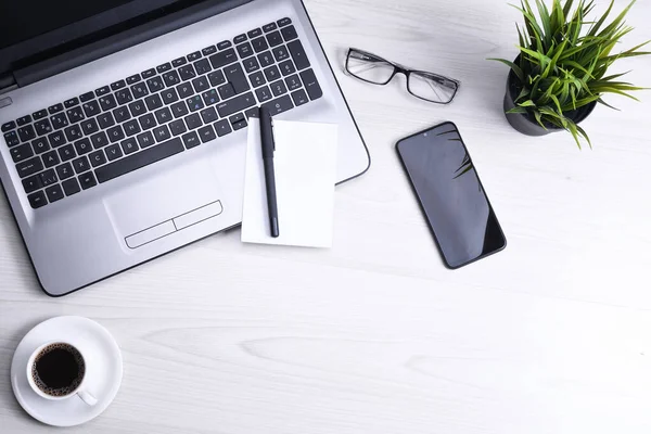 Ofis çalışma alanının en üst görüntüsü, dizüstü bilgisayarı, klavye kalemi, gözlükleri, telefonu, defteri ve kahveyi olan ahşap masa masası..