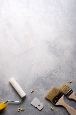 Gri beton arka planda boya yapmak için macun, fırça ve silindirler kullanılıyor. Üst görünüm