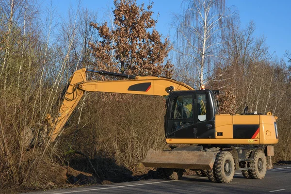 A bucket excavator clears the roadside. Road works. Laying a new road. Loading excavator clay and a stones