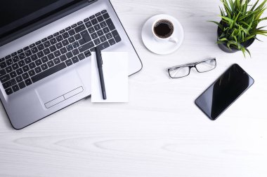 Ofis çalışma alanının en üst görüntüsü, dizüstü bilgisayarı, klavyesi, gözlükleri, telefonu ve bir fincan kahvesi olan tahta masa masası..