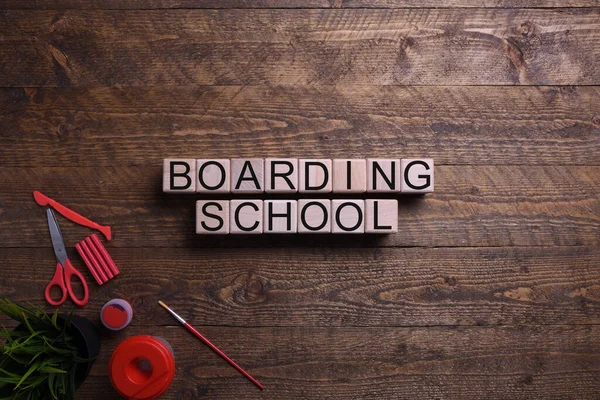 Word boarding school in wooden cubes, blocks on the subject of education, development and training on a wooden background. Top view. Place for text