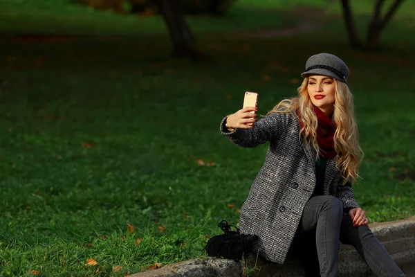 Belle femme est assise sur la route et de prendre selfie avec smartphone dans le parc d'automne — Photo