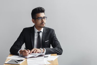 Bir not defteri ve görünüyor uzakta kameradan gri bir arka plan, tablet, telefon ve kağıtları masanın üzerine yazma iş adamı. kopya alanı