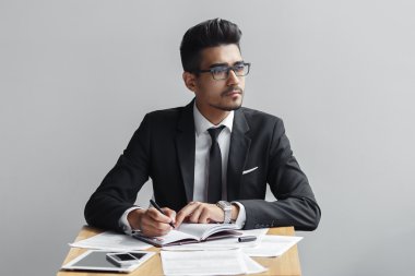 Bir dizüstü bilgisayar ve uzak görünüyor kamera, tablet, telefon ve kağıtları masaya yazma işadamı.