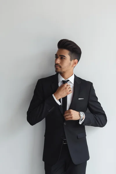 Hacer que los negocios se vean bien. Joven confiado en ropa formal ajustando su corbata y mirando hacia otro lado mientras está de pie sobre un fondo gris — Foto de Stock