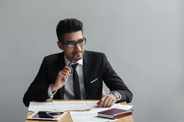 Geschäftsmann lächelt mit Stift auf grauem Hintergrund, Tablet, Telefon und Papier auf dem Tisch. — Stockfoto