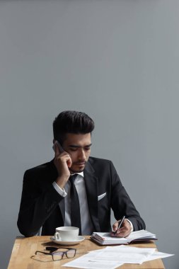 Güzel bir başarılı adam telefon ofis üzerinde konuşmak ve kafede bir defter yazma