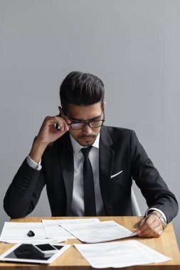 gri arka plan üzerinde ofis masasında otururken onun belgelerini seyir gözlüklü başarılı adam