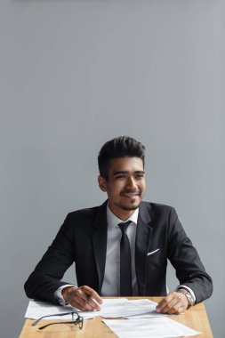 Yakışıklı genç iş adamı gülümseyen, işadamı gri arka plan üzerinde izole belgelerle çalışma