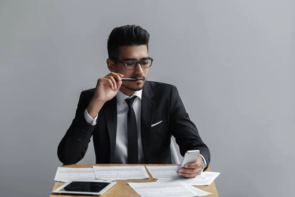 Empresário olhando para o telefone celular com uma caneta na boca — Fotografia de Stock