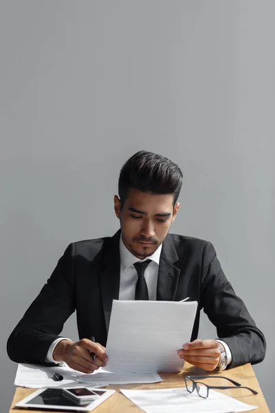 Porträt eines professionellen Geschäftsmannes, der auf seinem Schreibtisch auf grauem Hintergrund seine Dokumente betrachtet — Stockfoto