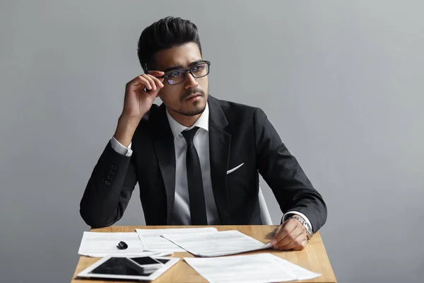 Succesvolle man met bril op zoek uit de buurt van de camera, de tablet, telefoon en papieren op de tafel. — Stockfoto