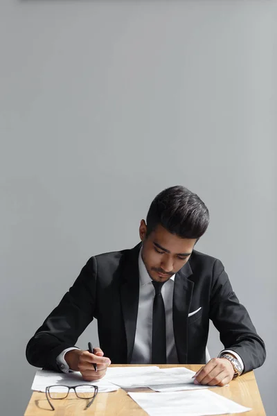 Όμορφος νεαρός επιχείρηση άνθρωπος γραφή, επιχειρηματίας που εργάζεται με έγγραφα υπογράψουν συμβόλαιο, κάθεται στο γραφείο του στο γραφείο, φορούν κομψά κοστούμι και γραβάτα που απομονώνονται σε γκρι φόντο — Φωτογραφία Αρχείου