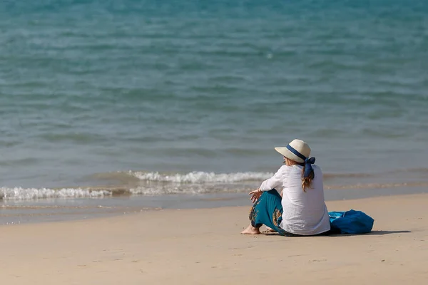 Mujer joven sentada en una playa de arena y mirando un mar azul oscuro —  Fotos de Stock