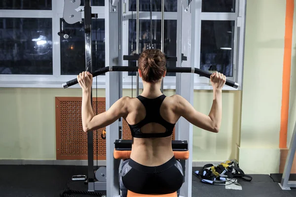 Unga Fitness kvinna som arbetar tillbaka på maskin i gymmet — Stockfoto