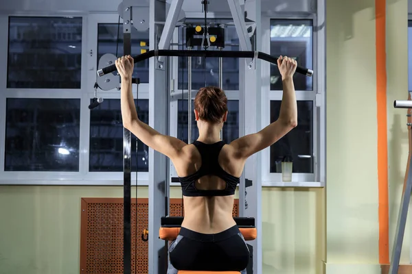 Jovem mulher se exercitando de volta na máquina no ginásio e músculos flexantes Modelo de aptidão muscular atlético fisiculturista — Fotografia de Stock