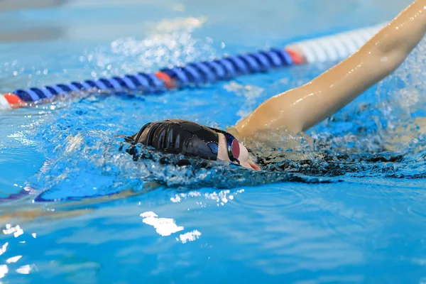 Jonge vrouw in bril en GLB borstcrawl lijnstijl in het blauwe water binnen race zwembad zwemmen. Stockafbeelding
