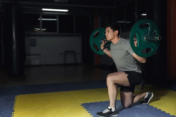 sport, bodybuilding, lifestyle and people concept - young man with barbell flexing muscles and making shoulder press lunge in gym.