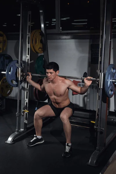 Bir halter ile çömelme vücut geliştiricisi. Vücut geliştirmeci barbell ile çalışma. Fitness salonunda barbell ile ağız kavgası yapan erkek. Smith makinesinin içinde belgili tanımlık jimnastik salonu. Spor salonunda Fitness adam. Mükemmel sağlıklı rakam.