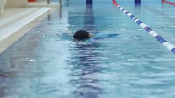 Junges Mädchen mit Brille und Schirmmütze schwimmt Freestyle-Stil im blauen Wasserbecken. — Stockvideo