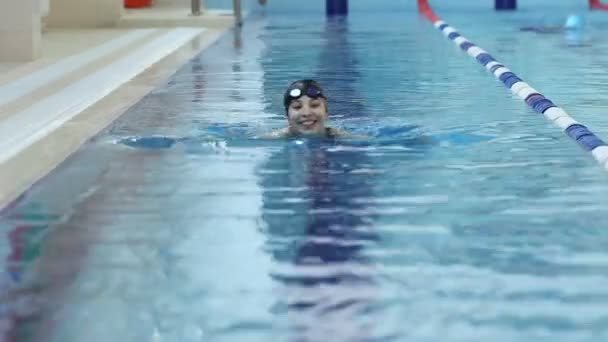 Jonge vrouw in bril en cap zwemmen in het zwembad van de indoor race blauw water. — Stockvideo