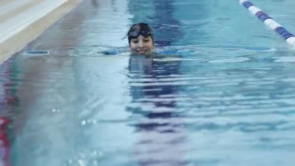 Mladá žena v brýle a čepici, koupání v bazénu vnitřní závod modrá voda. — Stock video