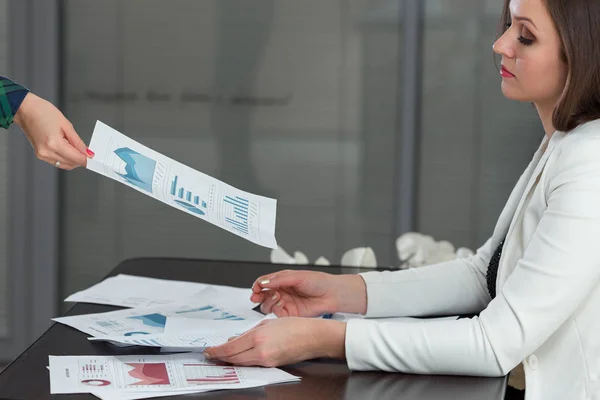 Cropped image of businesswoman giving progress chart to colleague at desk in office.
