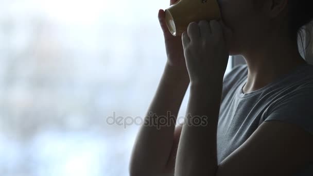 Young woman drinking coffee by the window during sunrise in her cozy home. — Stock Video