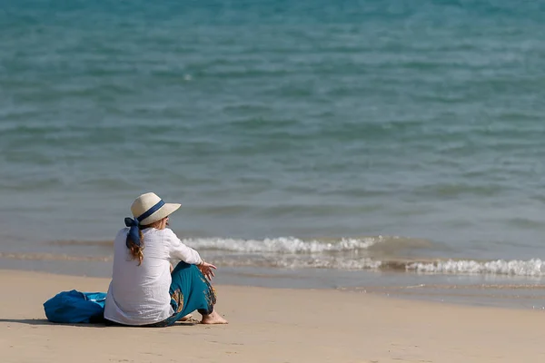 Mujer joven sentada en una playa de arena y mirando un mar azul oscuro . —  Fotos de Stock