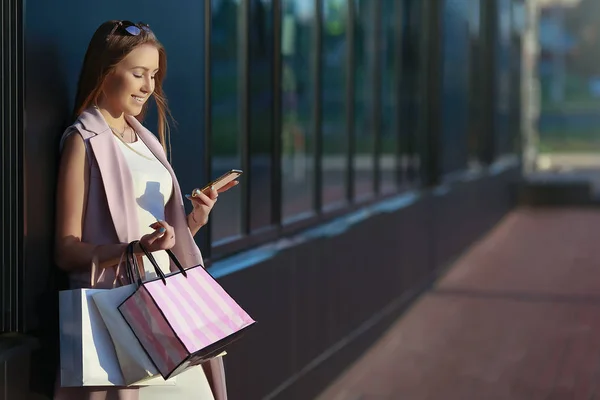 Mosolygó lány bevásárló táskák, és keresi a telefon — Stock Fotó