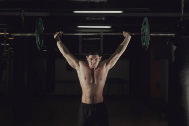 Spor salonunda halter kaldıran kaslı bir adam..