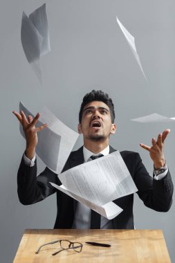Genç işadamı bazı kağıt sayfalarının gri arka plan üzerine atma.