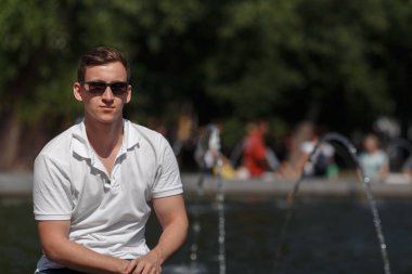 güneş gözlüğü çeşme yakınında oturan yakışıklı adam