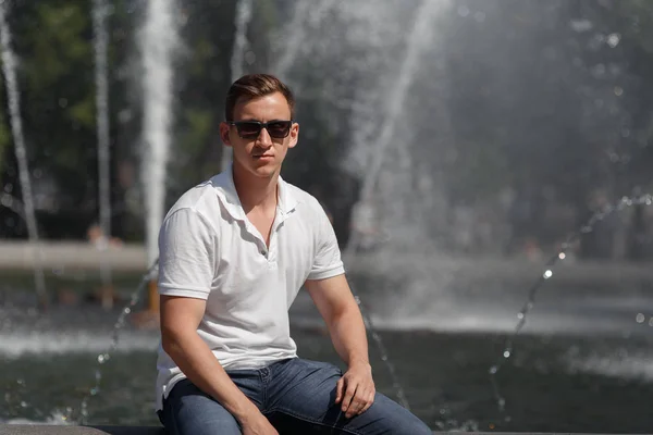 Красивый мужчина сидит в солнечных очках возле фонтана — стоковое фото