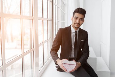 Pencere hediye kalp şeklinde ile oturan aşık genç işadamı.