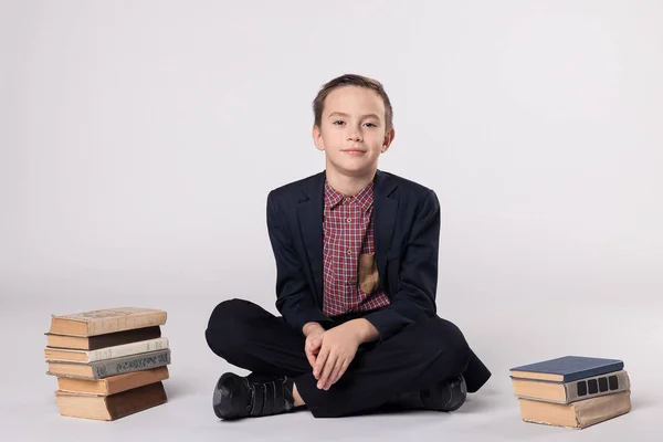 Niño lindo en un traje sentado y leyendo un libro sobre un fondo blanco —  Fotos de Stock