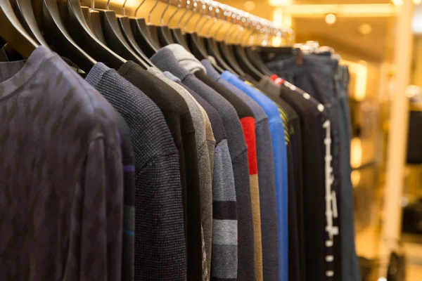 Hombres suéteres y camisas en diferentes colores en perchas en una tienda de ropa al por menor — Foto de Stock