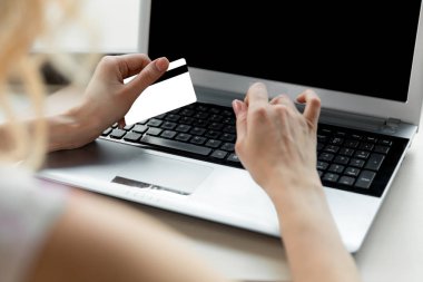 Yakın plan bir kadının elleri bir kredi kartı tutuyor ve online alışveriş için bilgisayar klavyesi kullanıyor..