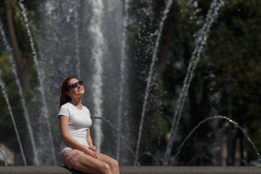 Güzel kadın güneş gözlüğü çeşme arka plan üzerinde oturuyordu