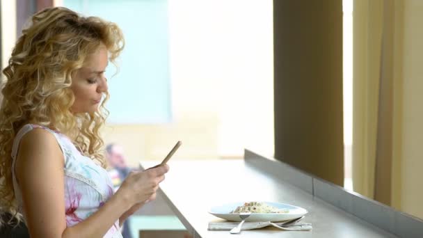 Jong blond meisje zelfportret maken op haar digitale camera van de smartphone zittend in café tijdens lunchpauze — Stockvideo