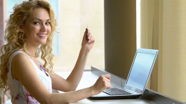 Mulher bonita segurando cartão de crédito na mão e inserindo código de segurança usando teclado laptop — Vídeo de Stock