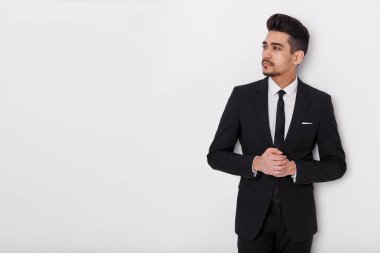 Beyaz bir arka plan üzerinde siyah elbiseli genç iş adamı. Kendine güvenen adam uzakta kameradan bakan.