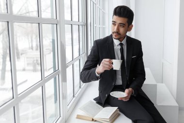 Düşünme işadamı pencere ve içecekler kahve üzerinde oturan takım elbiseli.